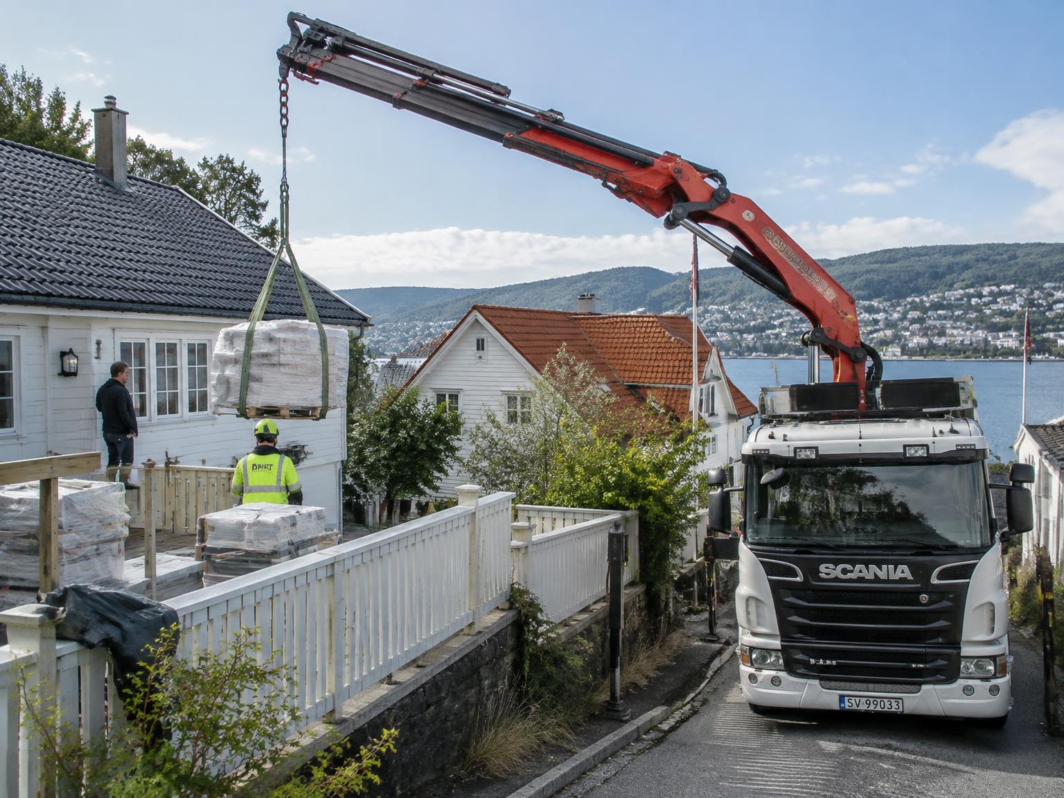 Kranbil leverer paller over et gjerde i et trangt boligområde (illustrasjon)